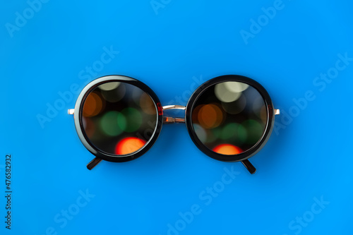 Minimalistic composition with sunglasses with multicolored bokeh in lenses, blue background, close-up © hannamartysheva