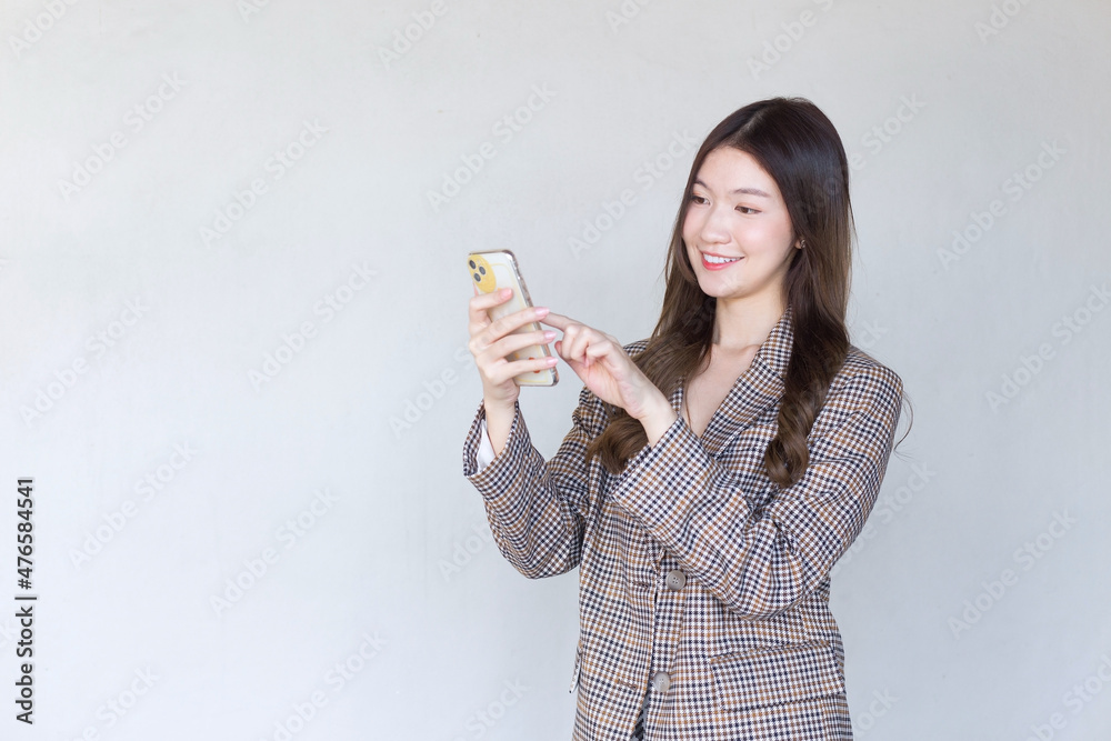 Asian professional woman with black long hair wearing a plaid suit and pretty happily using a smartphone on a white background. Asian professional woman with black long hair wearing a plaid suit and pretty happily using a smartphone on a white background.