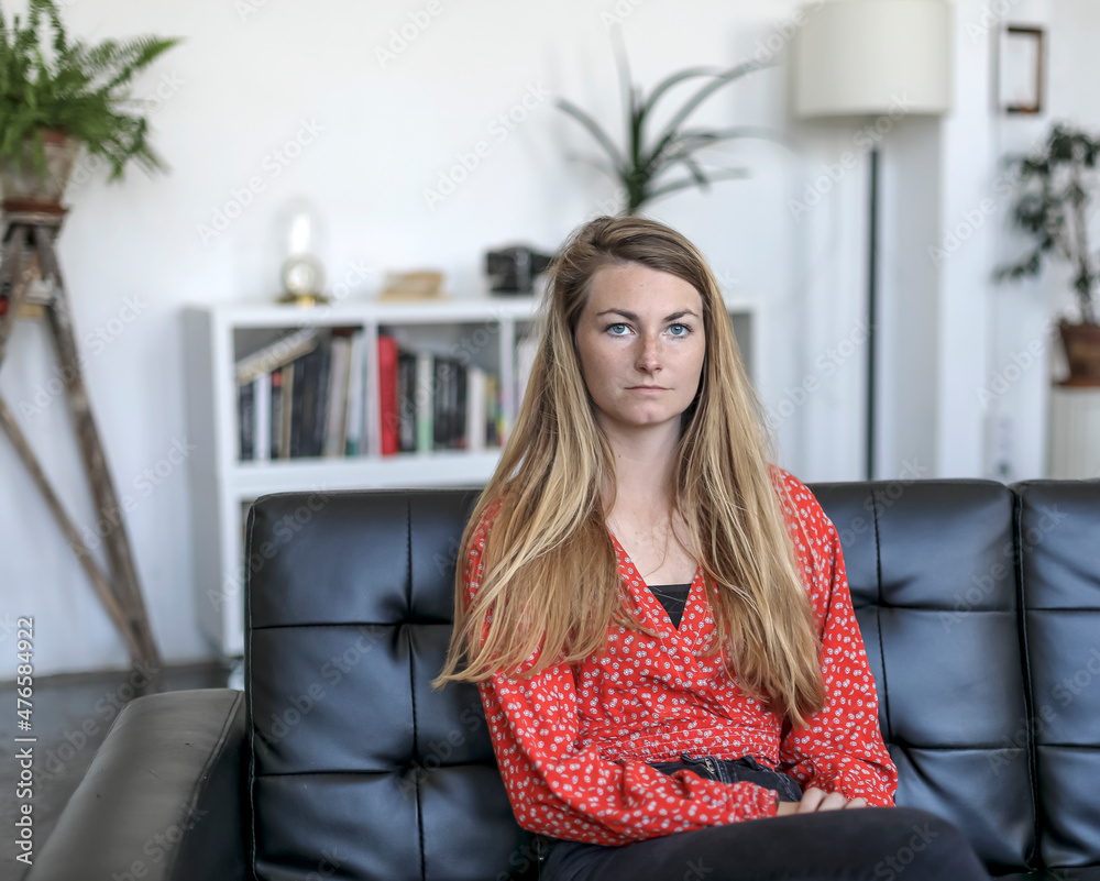 Young blond female relaxing on couch at home while looking away pensive Young blond female relaxing on couch at home while looking away pensive