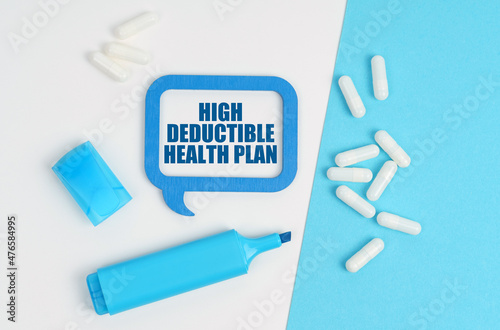 On a white and blue table are pills, a marker and a blue plaque with the inscription - High Deductible Health Plan