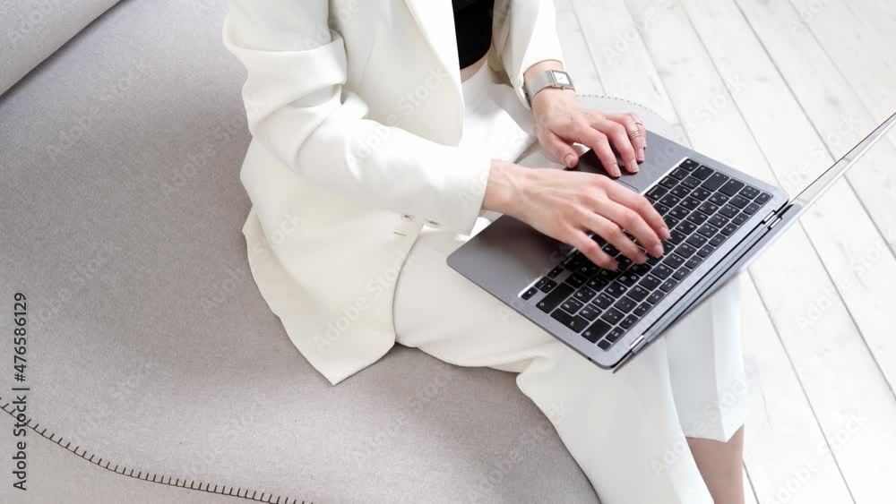 Female hands of a business woman texting on the laptop keyboard close-up on the background of the sofa. Business woman sending email to customer using digital wireless handheld device remotely Female hands of a business woman texting on the laptop keyboard close-up on the background of the sofa. Business woman sending email to customer using digital wireless handheld device remotely