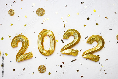 Gold glittering numbers 2022 on a white background strewn with sparkles and candy. New year concept. Flat lay, place for text.