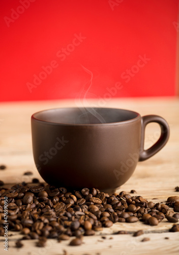 brown coffee cup with hot steam smoke and beans on wooden table  red background