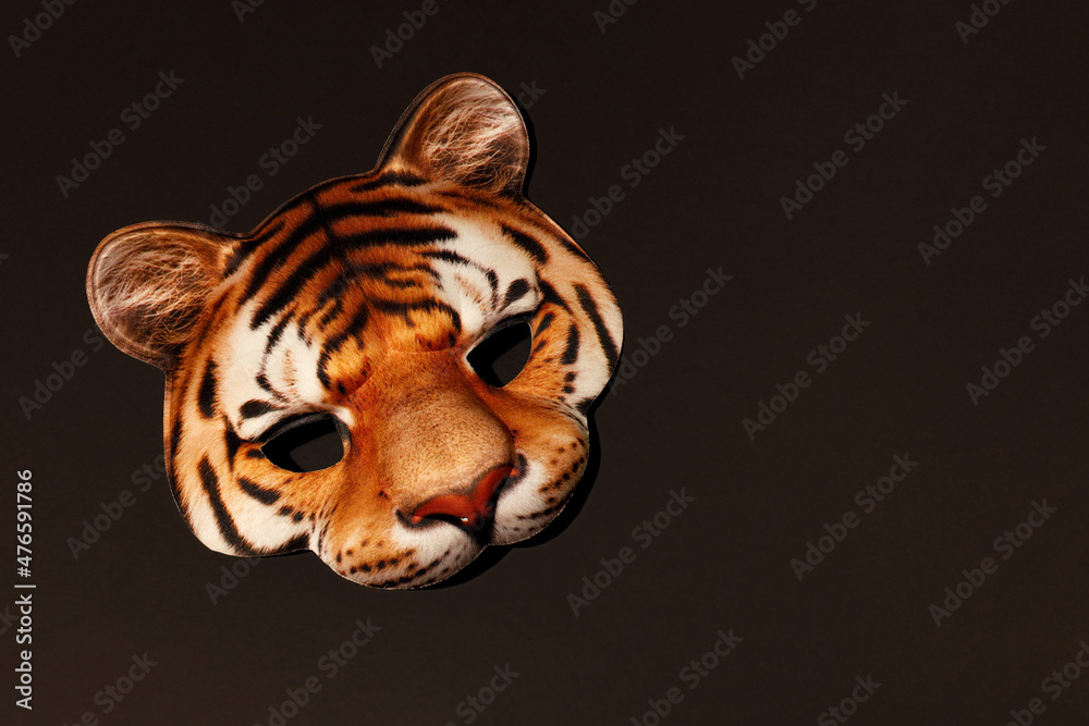 Orange Tiger striped masquerade face mask with realistic print of wildcat muzzle. Tiger is Symbol of 2022 New Year. Carnival kids mask for holiday party. Dark brown background with copy space.