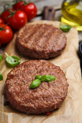 Tasty grilled hamburger patties with basil served on table, closeup