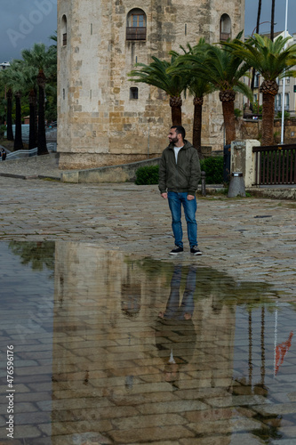 Chico joven realizando poses graciosas frente a un charco de agua situado frente a la Torre del Oro de Sevilla © Merijar