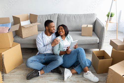 Excited black spouses with touch pad searching household goods for their new home, using tablet on moving day