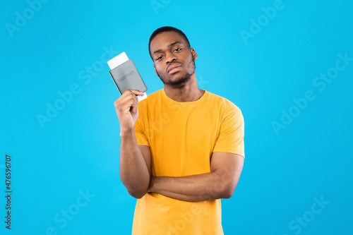 Discontented Black Tourist Man Holding Travel Tickets Over Blue Background