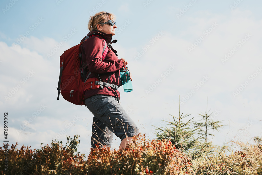 Woman with backpack hiking in mountains, spending summer vacation close to nature. Woman standing on top of hill admiring mountain landscape panorama holding bottle with water Woman with backpack hiking in mountains, spending summer vacation close to nature. Woman standing on top of hill admiring mountain landscape panorama holding bottle with water