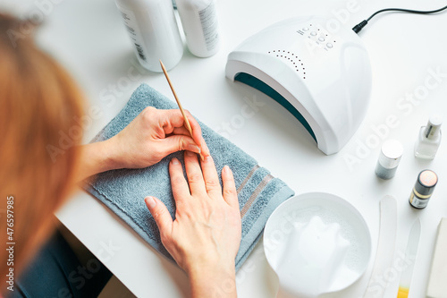 Woman preparing nails to apply gel hybrid polish using UV lamp. Beauty wellness spa treatment concept. Cosmetic products, UV lamp, green leaves on white table. Spa, manicure, skin care concept photo