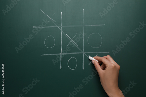 Woman playing tic tac toe game on green chalkboard, top view
