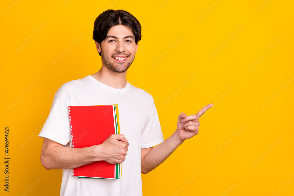 Portrait of attractive cheerful guy holding exercise book showing copy space ad isolated over bright yellow color background Portrait of attractive cheerful guy holding exercise book showing copy space ad isolated over bright yellow color background