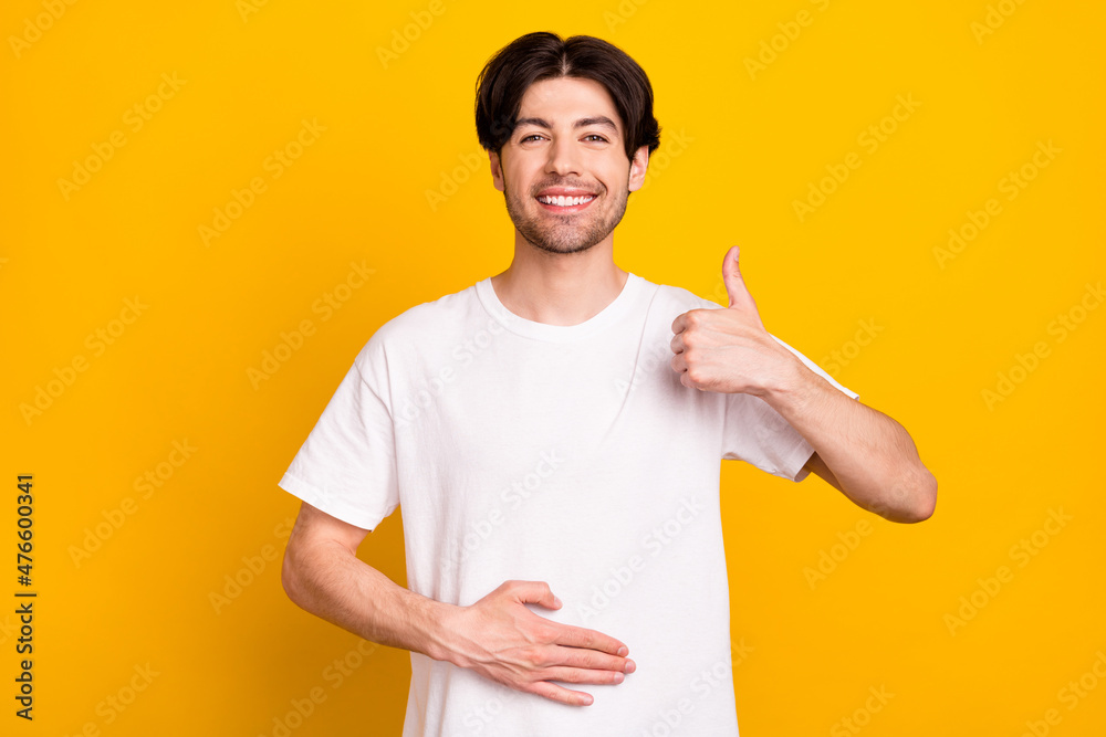 Photo of optimistic young guy show thumb up wear white t-shirt isolated on yellow color background Photo of optimistic young guy show thumb up wear white t-shirt isolated on yellow color background
