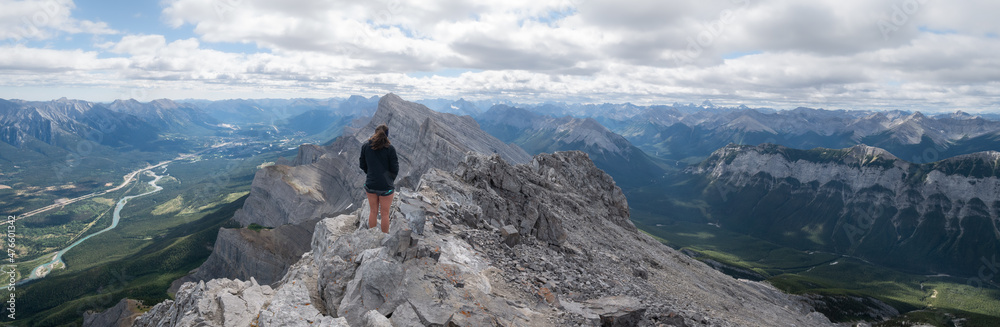 Wide panoramic shot of female hiker enjoying the views on valley from mountain summit