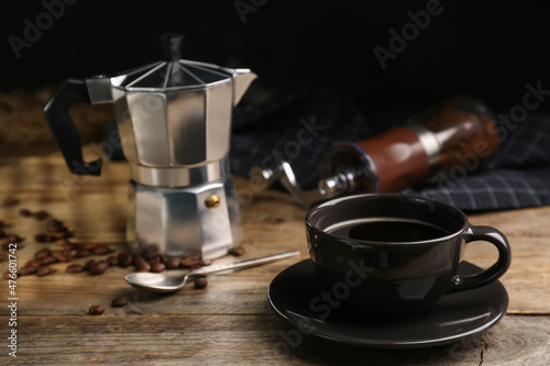 Cup of aromatic coffee, moka pot and scattered beans on wooden table. Space for text