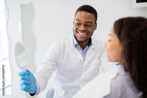 Black Dentist Doctor Holding Mirror, Showing Result Of Teeth Treatment To Patient