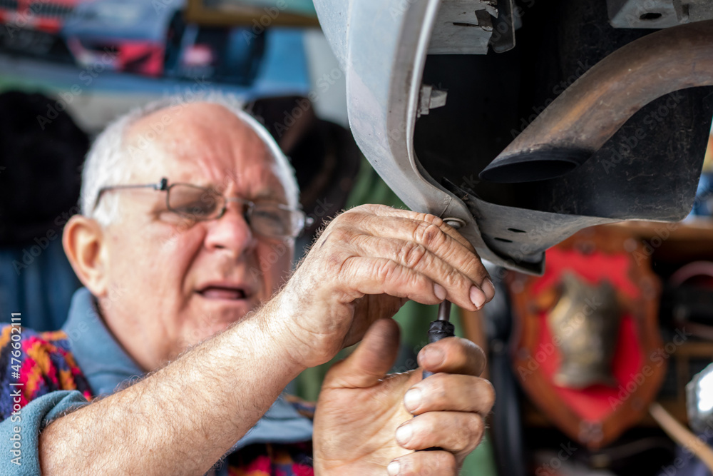 Portrait of an old car mechanic checking and repairing a lifted