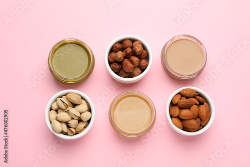 Different types of delicious nut butters and ingredients on pink background, flat lay