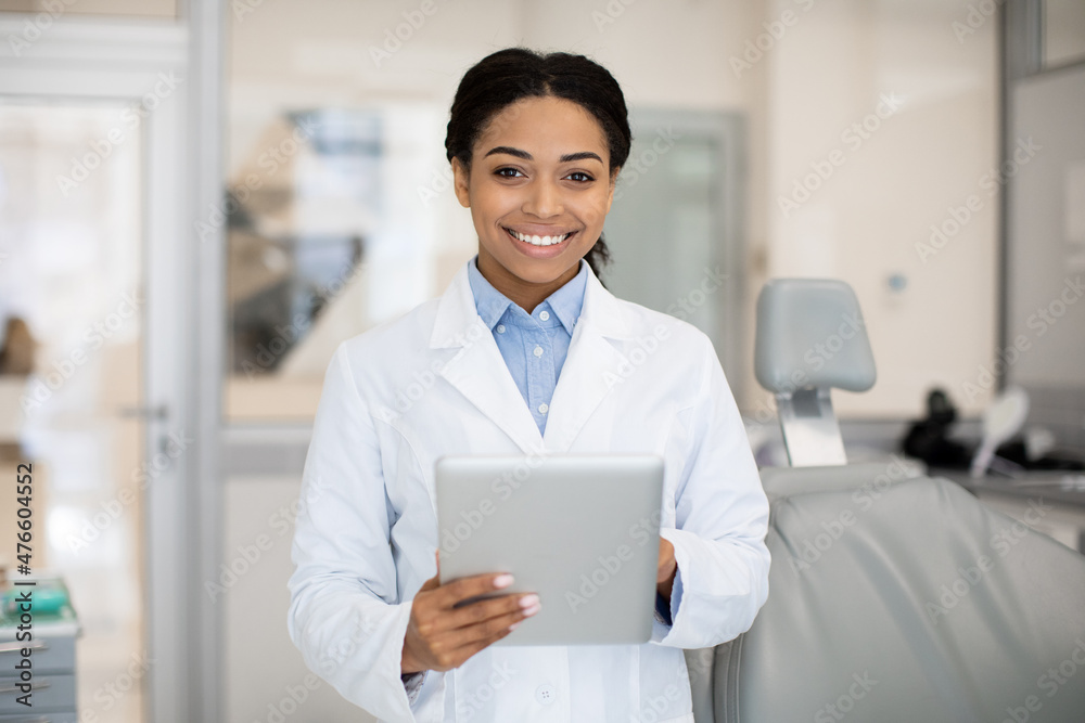 Smiling black female dentist doctor with digital tablet posing in stomatology clinic Smiling black female dentist doctor with digital tablet posing in stomatology clinic