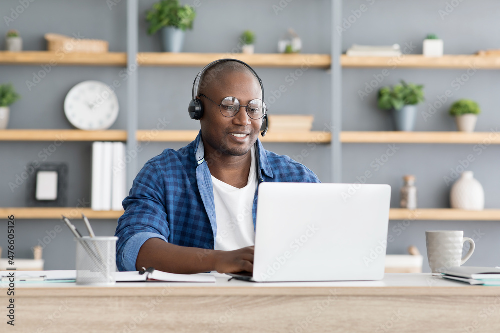 Hotline support service. African american male call center operator in headset working with laptop computer at home Hotline support service. African american male call center operator in headset working with laptop computer at home