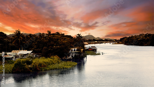 Dark contrast sunset in tropics on big river with village, bridge and mountains on background. The Bridge on the River Kwai, Thailand 5th of july 2009