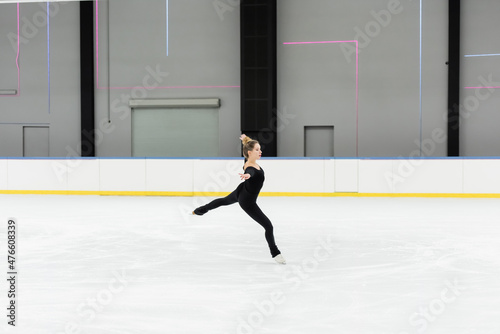full length of professional figure skater in bodysuit skating with outstretched hands in ice arena