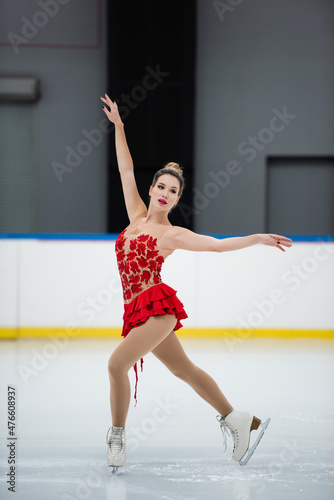 full length of woman in red dress figure skating with outstretched hands on ice rink