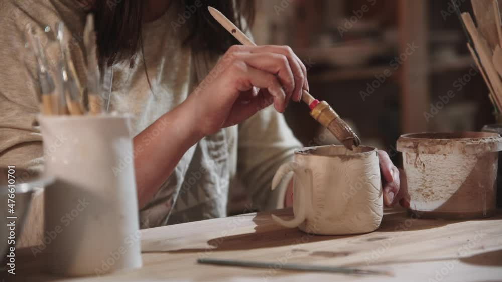 Young woman potter working in art studio - painting the final ceramic product from the inside Young woman potter working in art studio - painting the final ceramic product from the inside