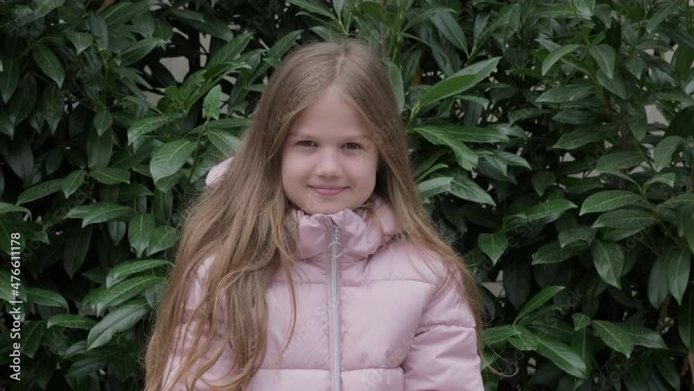 Portrait of little girl in pink jacket on background of green foliage. Kid smiling looking at camera. Child in the Park on Sunny spring or autumn Day. Face funny Kid outdoors. Portrait of little girl in pink jacket on background of green foliage. Kid smiling looking at camera. Child in the Park on Sunny spring or autumn Day. Face funny Kid outdoors.