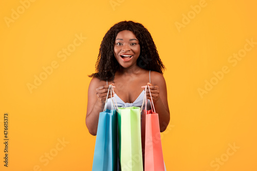 Excited black woman holding bright shopping bags, posing and looking at camera, happy with her summertime purchases