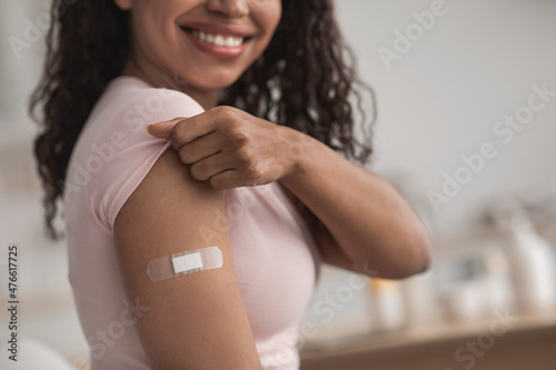 Фотография Happy young pretty african american female showing arm with band-aid after getti