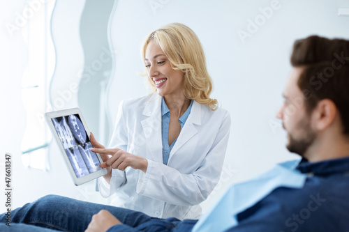 Female dentist showing man patient treatment goal  using tablet