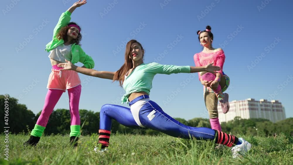 Happy confident sportswomen in retro sportswear stretching muscles warming up outdoors. Fit slim beautiful Caucasian women training exercising in 1990s on sunny summer meadow. Vintage sport concept