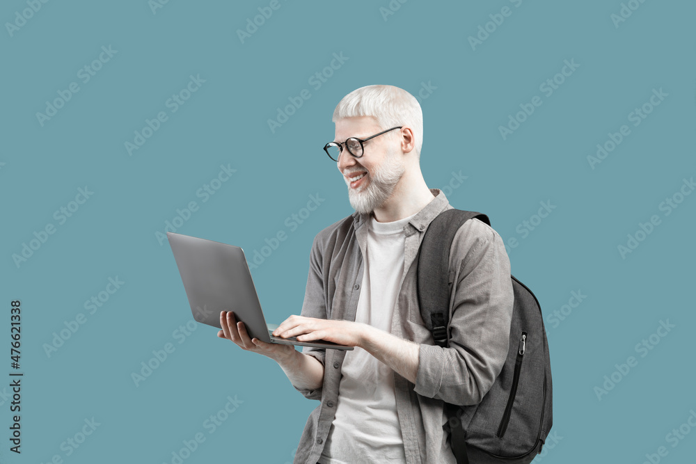 Cool guy with unusual appearance using laptop for online work or studies, wearing backpack over turquoise background Cool guy with unusual appearance using laptop for online work or studies, wearing backpack over turquoise background