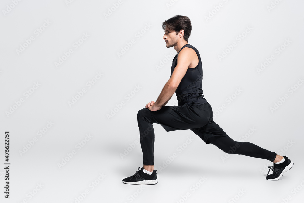 Side view of sportsman doing lunges on grey background