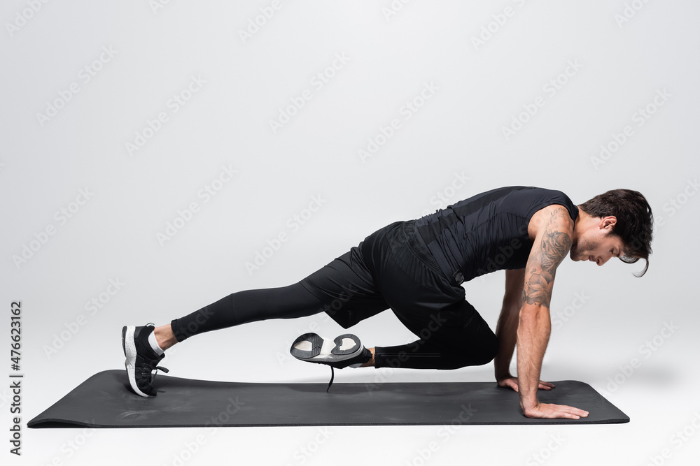 Obraz premium Side view of sportsman working out on black fitness mat on grey background