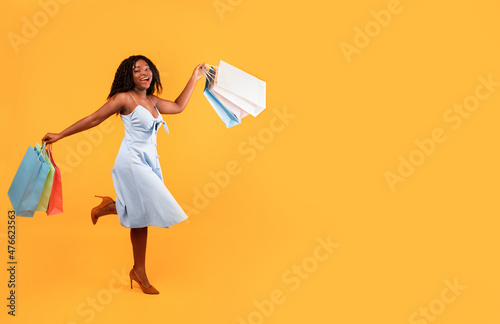 Big sales concept. Full length of young happy black woman running with colorful shopping bags over orange background
