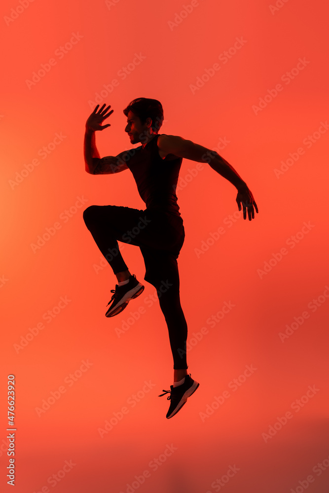 Side view of sportsman jumping on red background