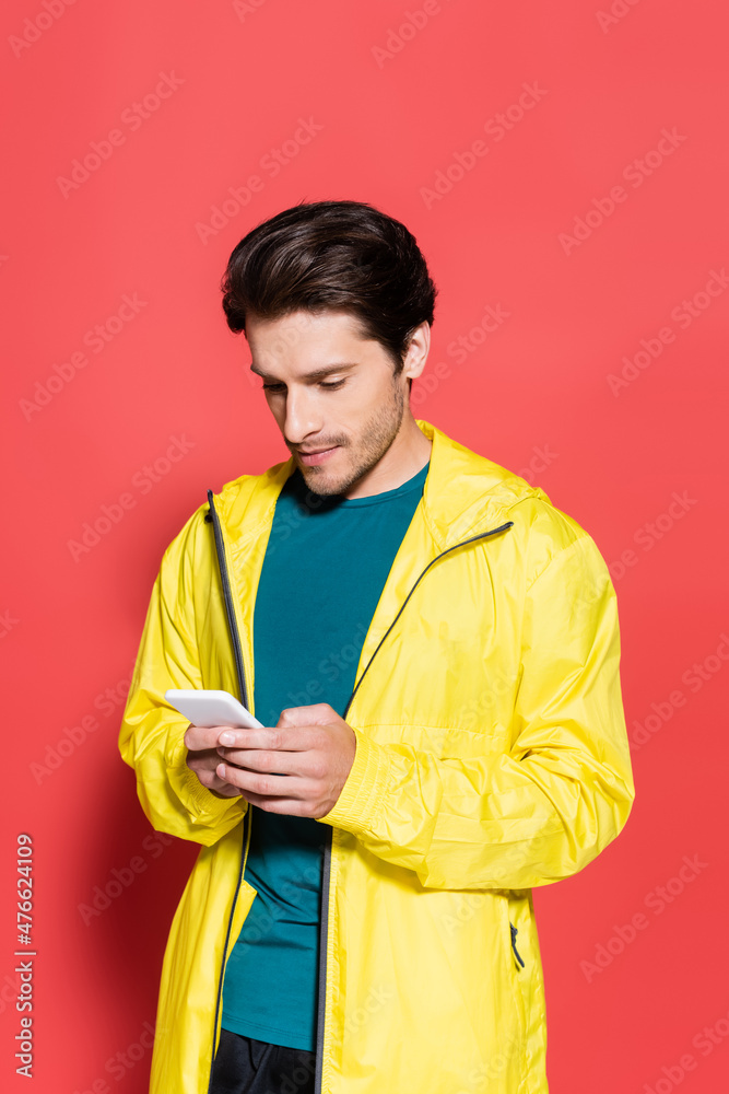 Sportsman in sports jacket using smartphone on red background Sportsman in sports jacket using smartphone on red background