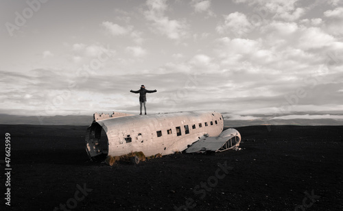 Man outstretching arms on crashed airplane on volcanic beach photo
