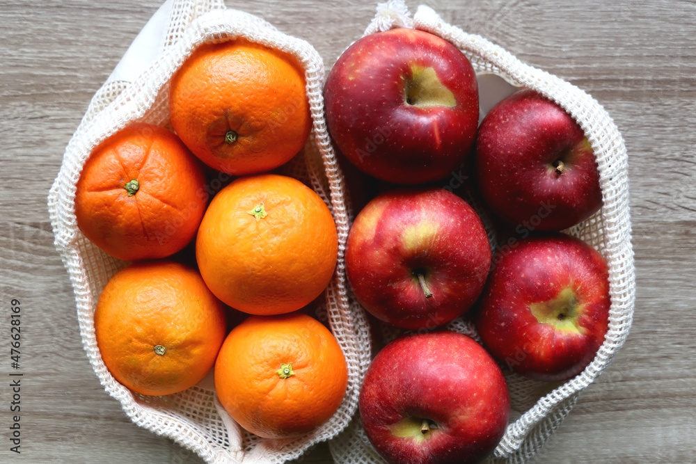 Two sustainable shopping bags filled with apples and oranges on wooden table. Top view. Two sustainable shopping bags filled with apples and oranges on wooden table. Top view.