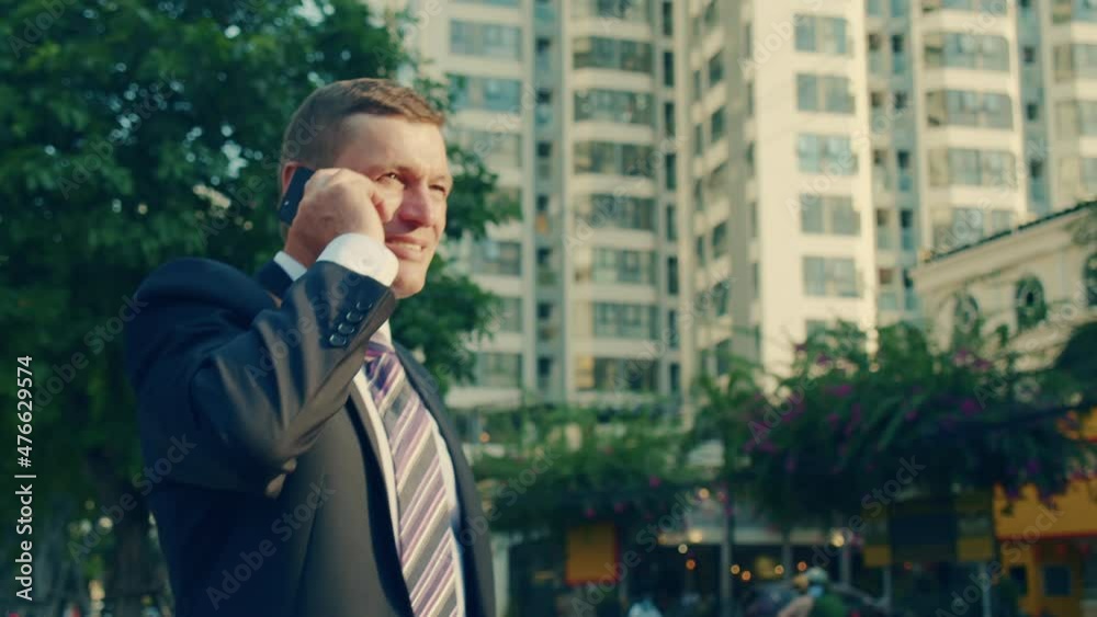 4k A man talking on a cell phone in the street. A smiling middle-aged businessman in luxurious clothes in the financial district of a metropolis uses a mobile phone for negotiations. 4k A man talking on a cell phone in the street. A smiling middle-aged businessman in luxurious clothes in the financial district of a metropolis uses a mobile phone for negotiations.