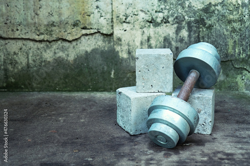 Sport mock up concrete cube empty podium with heavy metal dumbbell on grunge cement background. Abstract banner or minimal scene for fitness product presentation.