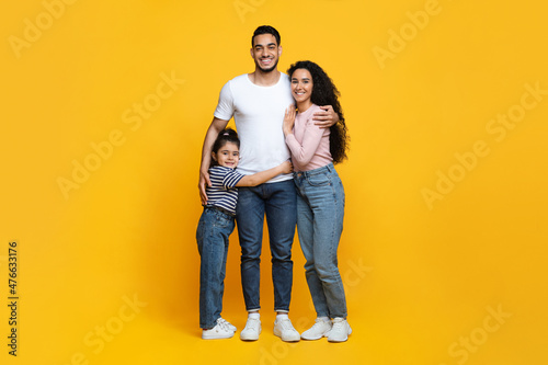 Family Portrait. Happy Arab Parents And Little Daughter Embracing Over Yellow Background © Prostock-studio