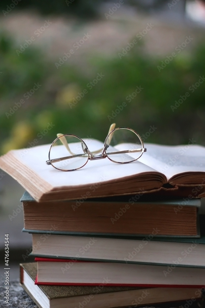 Stack of hardcover books and reading glasses in a garden. Selective focus. Stack of hardcover books and reading glasses in a garden. Selective focus.