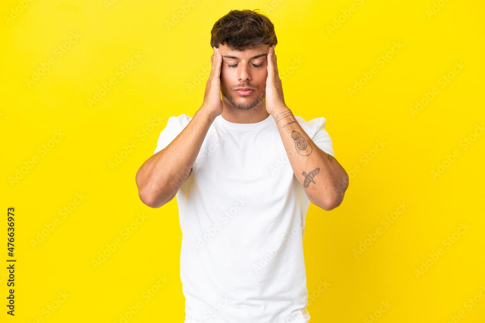Naklejka premium Young caucasian handsome man isolated on yellow background with headache