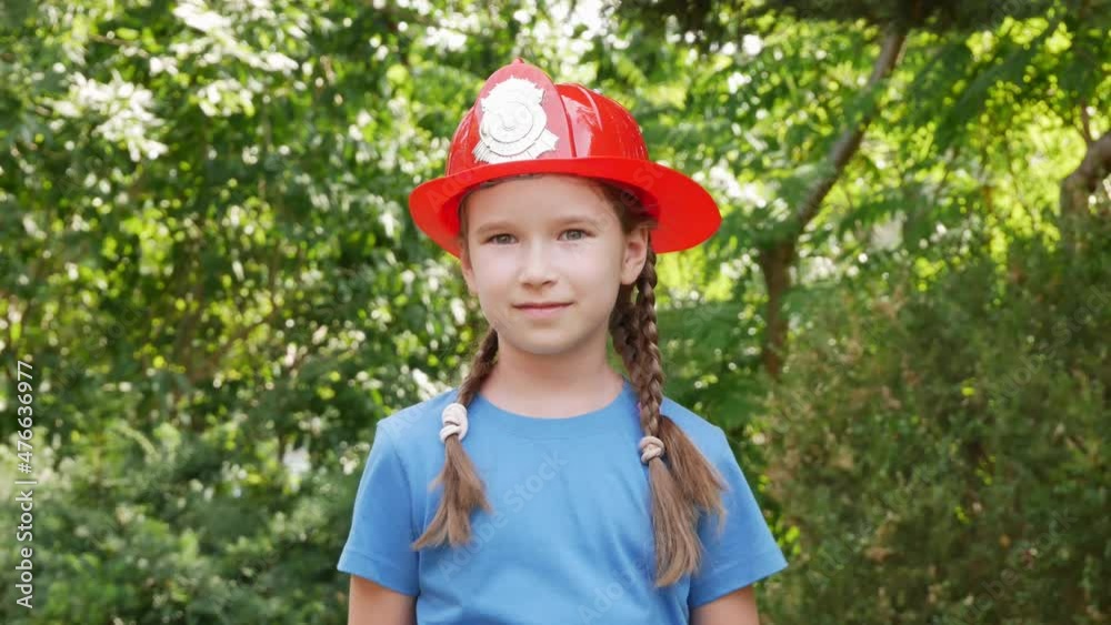 Elementary school age girl wearing red fireman toy helmet, child in a firefighter emergency service costume, portrait, face closeup, zoom in. Real people, jobs occupations, children dreams concept Elementary school age girl wearing red fireman toy helmet, child in a firefighter emergency service costume, portrait, face closeup, zoom in. Real people, jobs occupations, children dreams concept