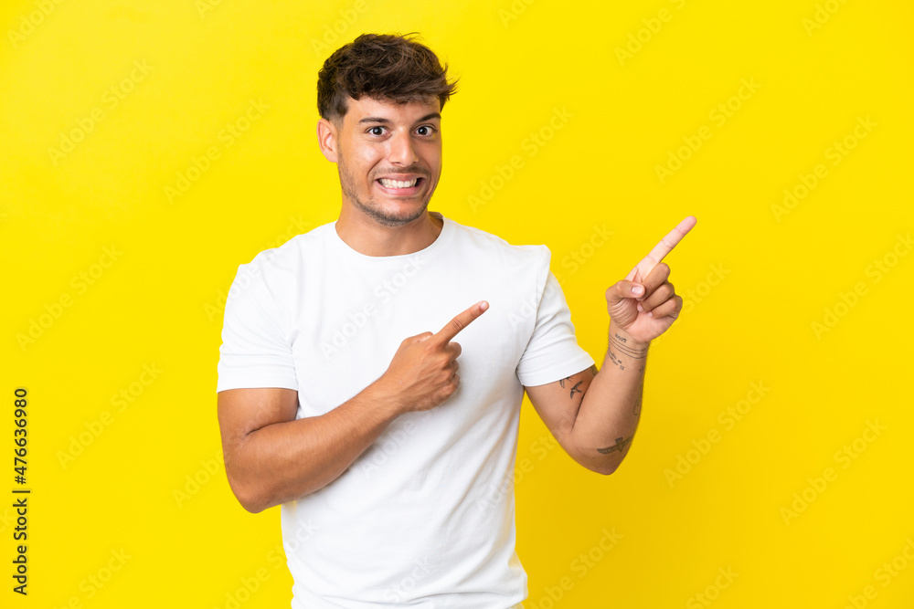 Young caucasian handsome man isolated on yellow background frightened and pointing to the side