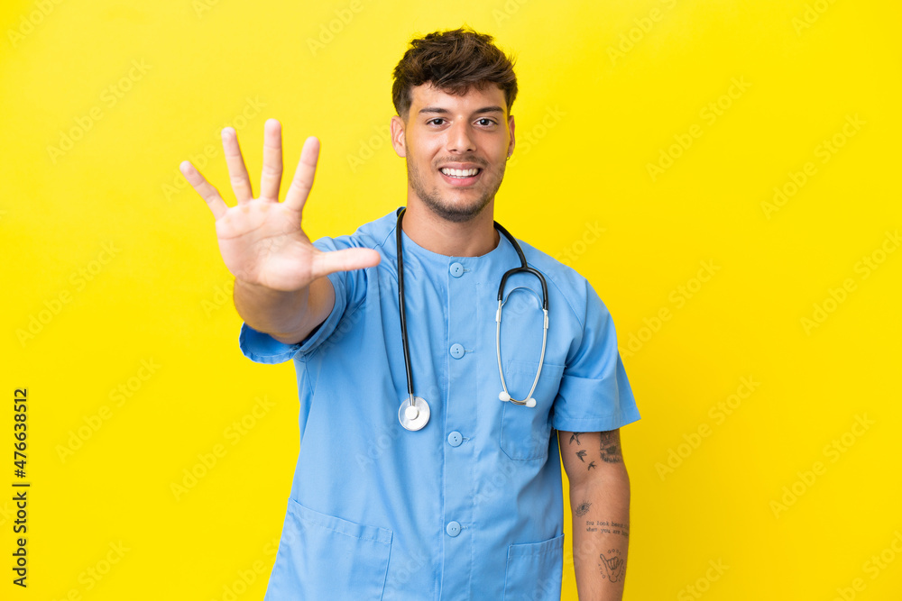 Young surgeon doctor man isolated on yellow background counting five with fingers Young surgeon doctor man isolated on yellow background counting five with fingers