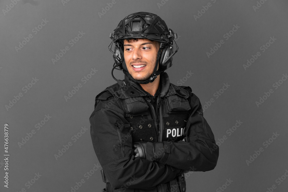 SWAT caucasian man isolated on grey background with arms crossed and happy SWAT caucasian man isolated on grey background with arms crossed and happy